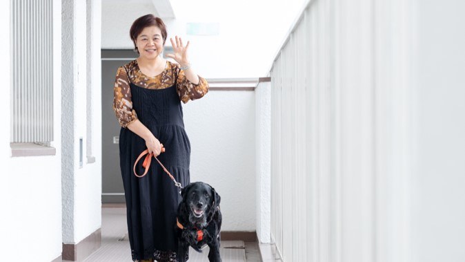 マンションの廊下にいる安藤さんと聴導犬のアーミちゃん