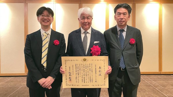 胸章をつけた3人。真ん中に賞状を持つ大沼理事長。